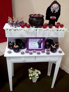 a white table topped with lots of cups and vases filled with liquid next to a doll