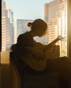 a woman sitting on a window sill playing a guitar