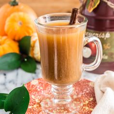 a glass cup filled with liquid and cinnamon on top of a table next to pumpkins