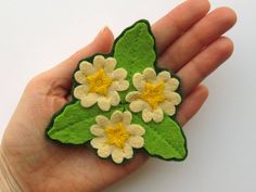 a hand holding a green and white flower brooch