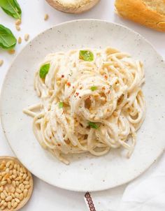 a white plate topped with pasta next to bread and green leafy garnish