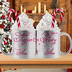 two mugs with candy canes on them sitting in front of a christmas tree