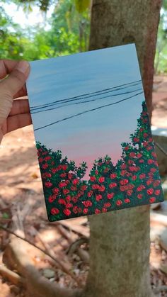 a hand holding up a piece of paper that has been painted with flowers on it