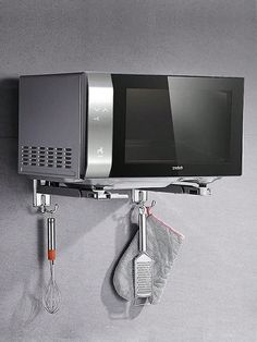 a microwave mounted to the side of a wall with cooking utensils hanging from it