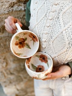 a woman holding two cups in her hands with flowers painted on the cup and saucer