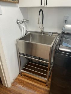 a stainless steel sink and washer in a small room with wood floors, white walls and cabinets