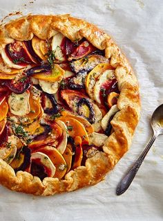 a pie with fruit and herbs on it sitting next to a silver spoon, fork and napkin