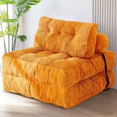 an orange couch sitting on top of a wooden floor next to a potted plant