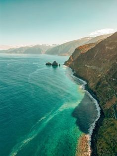 an aerial view of the ocean with mountains in the background and blue water on either side