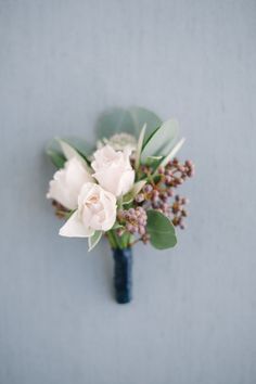 a boutonniere with white flowers and greenery on a blue wall background