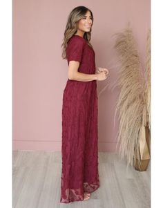 a woman standing in front of a pink wall wearing a red dress and smiling at the camera