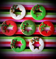 six decorated doughnuts arranged in the shape of christmas wreaths on a striped background