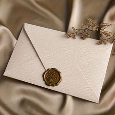 an envelope with a wax stamp on it sitting on a satin surface next to some flowers