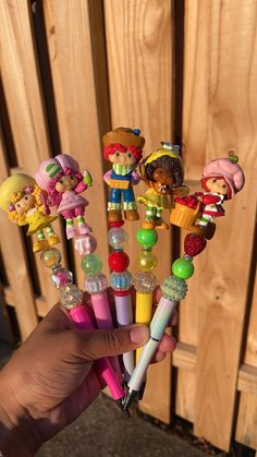 a person holding several different colored pens in front of a wooden fence with cartoon characters on them