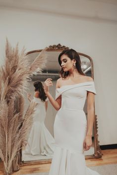 a woman standing in front of a mirror wearing a white dress