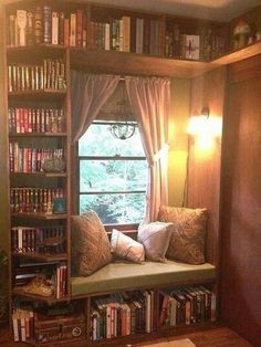 a window seat in front of a book shelf filled with lots of books and pillows