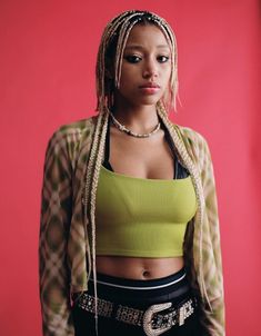 a woman with dreadlocks standing in front of a red wall wearing a green top