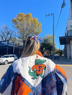 a woman in an orange, white and blue jacket is walking down the street with her back to the camera