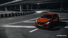 an orange car is driving down the road at night time in front of a bridge