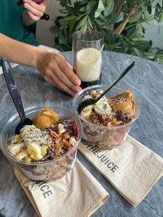 two desserts in plastic containers with spoons on napkins next to a glass of milk