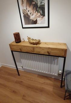 a wooden table sitting next to a wall with a painting on the wall above it