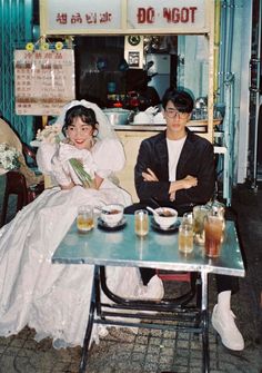 two people sitting at a table with drinks in front of them and one person wearing a wedding dress