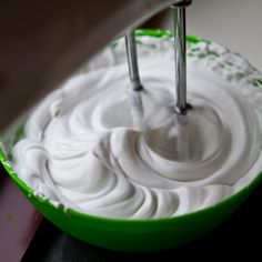 a green bowl filled with white frosting on top of a table