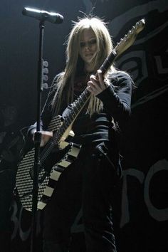 a woman with long blonde hair holding a guitar in front of a microphone on stage