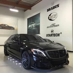 a black mercedes s - class is parked in a showroom with white walls and flooring