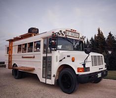 a white school bus parked on top of a parking lot next to trees and grass