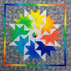 a quilted wall hanging with multicolored stars and leaves in the center, on a gray background