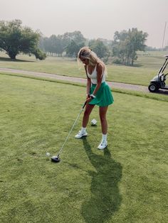 a woman in a green skirt is playing golf on the grass with her putter