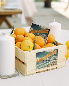 a wooden crate filled with oranges on top of a table next to a candle