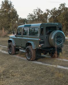 a green jeep driving down a dirt road next to some grass and trees in the background