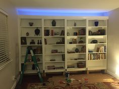 a living room filled with lots of white bookshelves next to a lamp and window