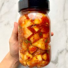 a hand holding a jar filled with food on top of a table next to a marble counter