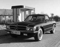 a black and white photo of a mercedes parked in front of a gas station,