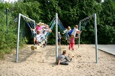 children are playing in the sand on a swing set with trees in the back ground