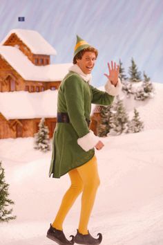 a man dressed as elf riding on top of a snow covered ski slope in front of a house