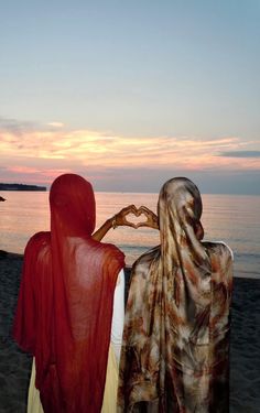 two people sitting on the beach with their backs to each other