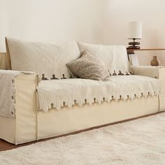 a white couch sitting on top of a wooden floor next to a lamp and rug