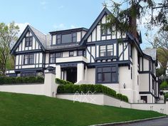 a large white and black house on the side of a hill in front of some trees