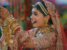 a woman in a red and gold bridal outfit is holding something up to her face