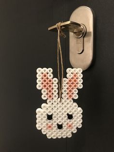 a white and pink beaded bunny hanging from a hook on a black wall next to a light switch