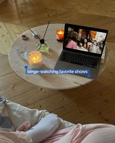 a laptop computer sitting on top of a wooden table next to a cup and candle