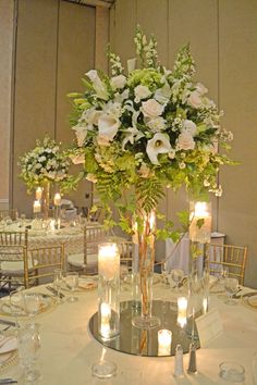 an elegant centerpiece with white flowers and greenery is displayed on a round table