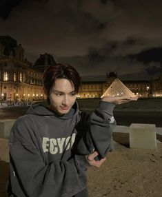 a young man holding up a crystal pyramid in front of a large building at night