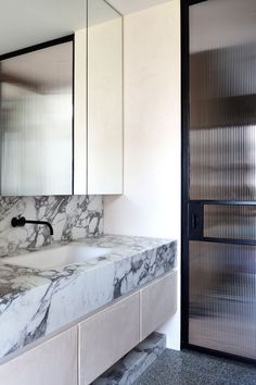 a bathroom with marble counter tops and white cabinetry next to a glass sliding door