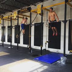 two men hanging upside down on the ropes in a crossfit gym with blue mats