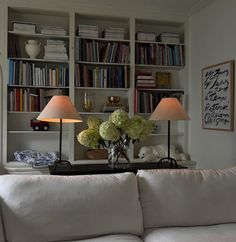 a living room filled with white furniture and bookshelves covered in lots of books